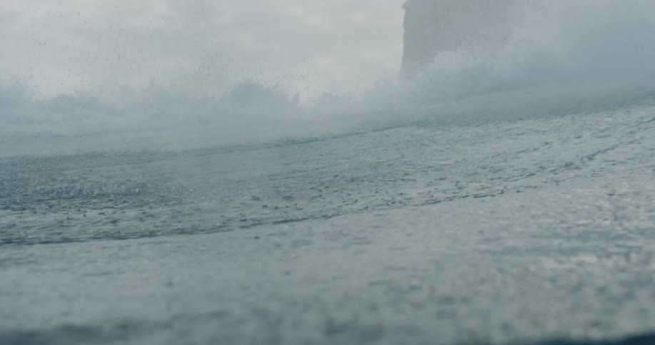 A rough sea with waves breaking on a mountain causing small drops of water to fall on the surface