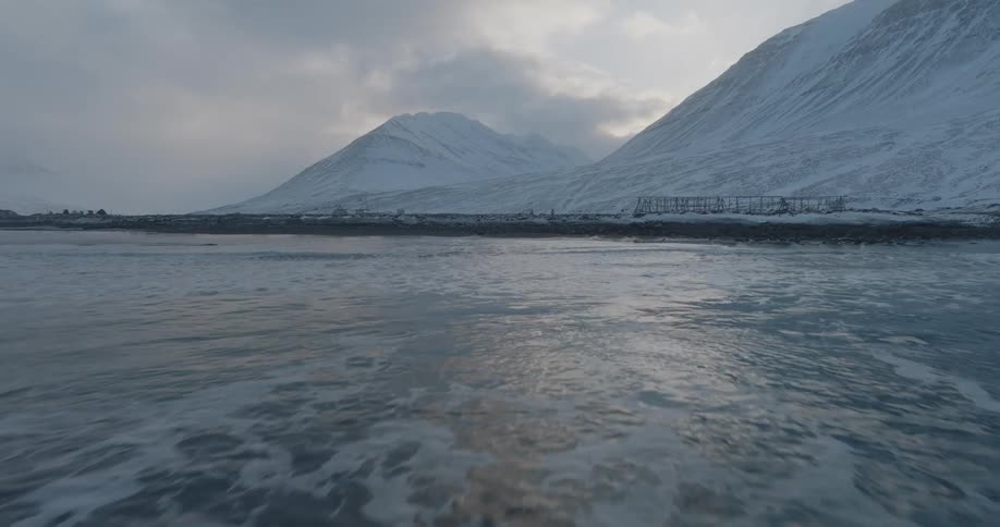 Moving over the icy water toward the shore and snow covered mountains under a cloudy sky