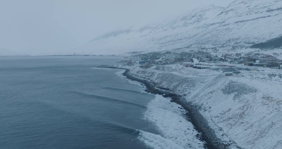 View of the sea coast with the village and snowcovered mountains just behind