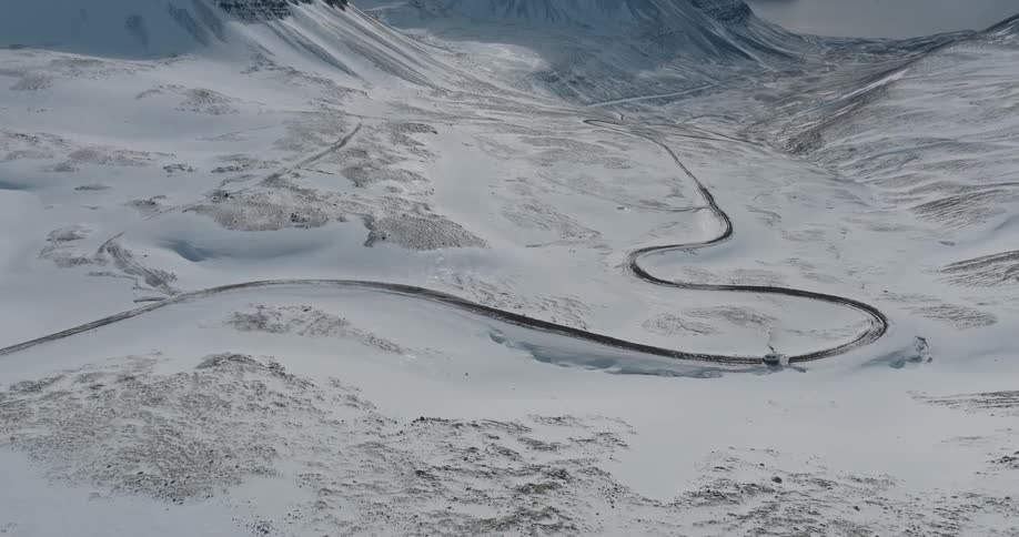 A van travels on a winding road through a snow covered mountain valley
