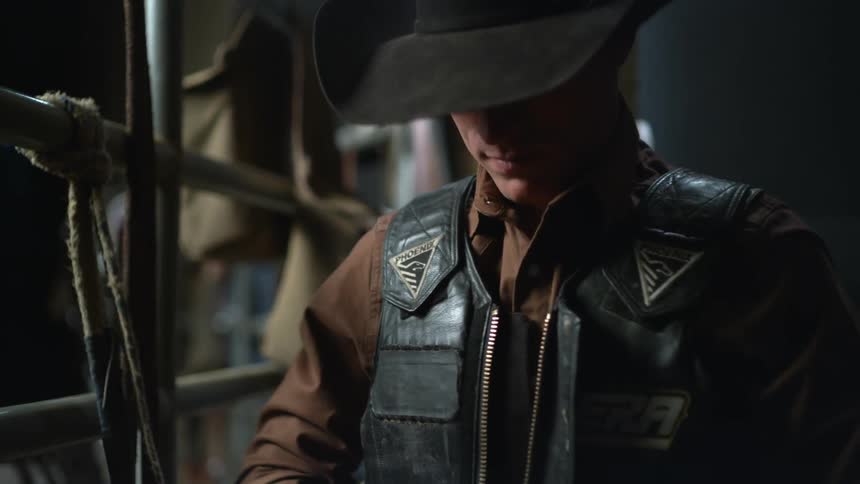 A rodeo cowboy puts on and zips up his safety vest