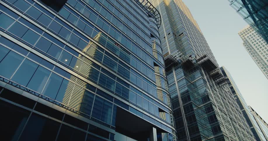 A tall building reflects on the windows of another downtown building