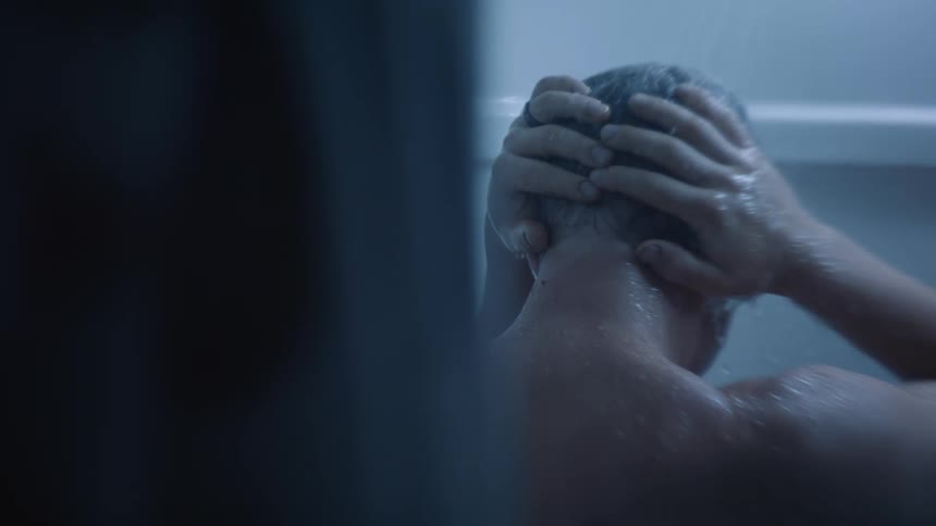 Closeup of a mans back taking a shower with both hands on his head in a depressive manner