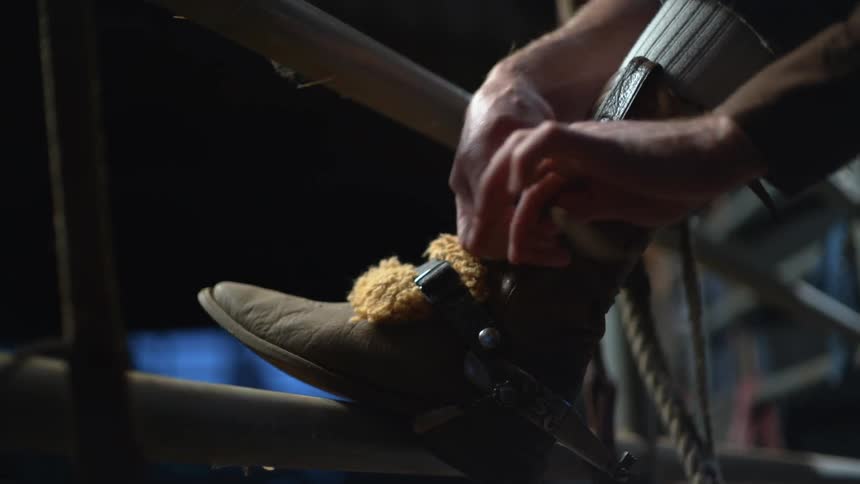 Cowboy strapping on his boots at a rodeo