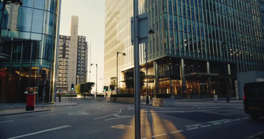 A van is parked on the side of a downtown street as a man walks on the sidewalk and the sun shines on buildings