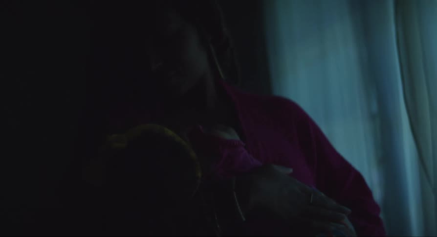 A woman rocks a sleeping baby in her arms in a dark room during the day