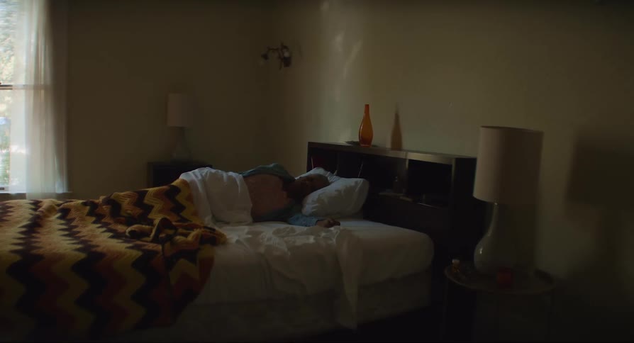 Man lies on his side on bed near window