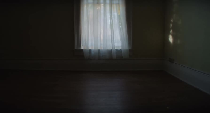 View of an empty indoor room with no furniture and a white curtain on the window