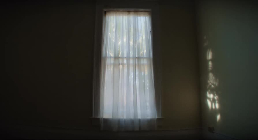 A curtain waving slightly in an empty dark room