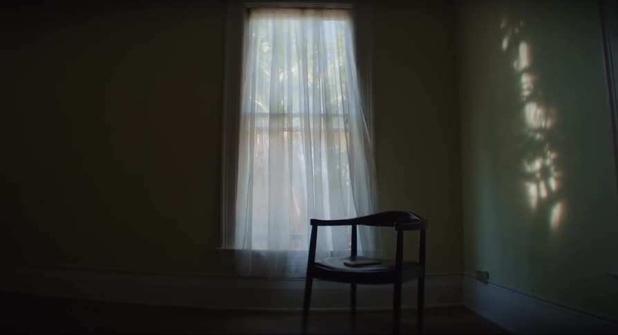 Room with a central chair and a window in the background with a white curtain