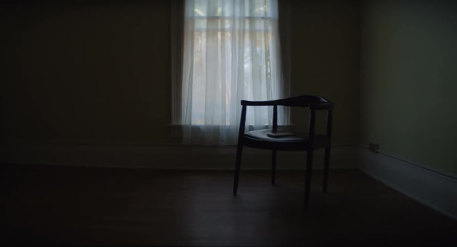 An empty room with a wooden chair by the window