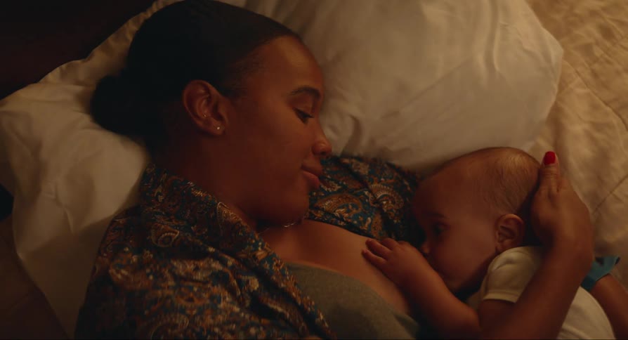 Mother lies on bed and strokes and breastfeeds her baby