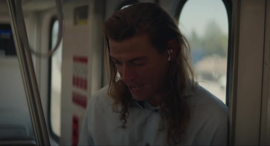A man on a train uses earbuds while on a smart phone