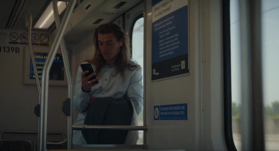 Man inside public transportation taking his cellphone out of his pocket and smiling as he reads something