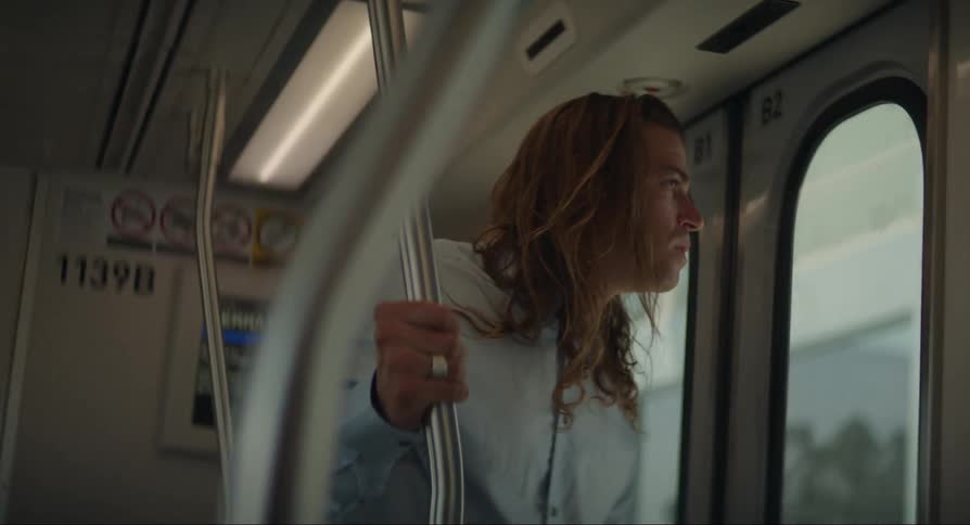 A man with long hair is on the train and looks at his cell phone and then leaves