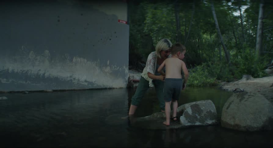 Mother helping her son to take off his shoes while standing on a rock in a lake