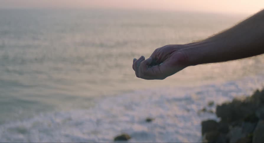 Mans hand holding sand on the beach near the sea