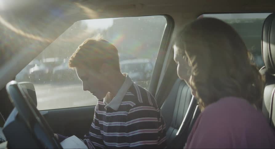 Mother and son sitting in parked car hug and smile after he reads letter with good news