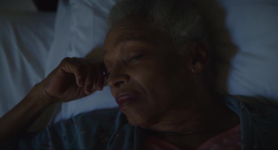Elderly woman lying in bed with one hand on her face and a look of sadness