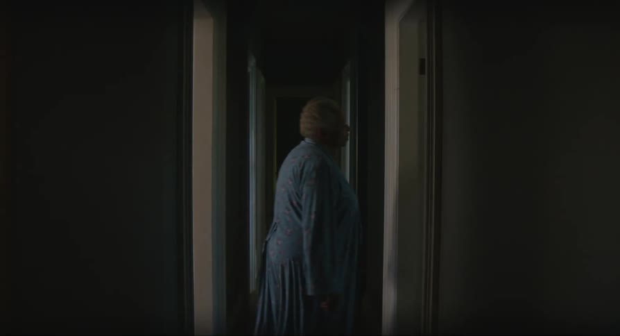 A long dark hallway in a home as a woman walks from one doorway to the next