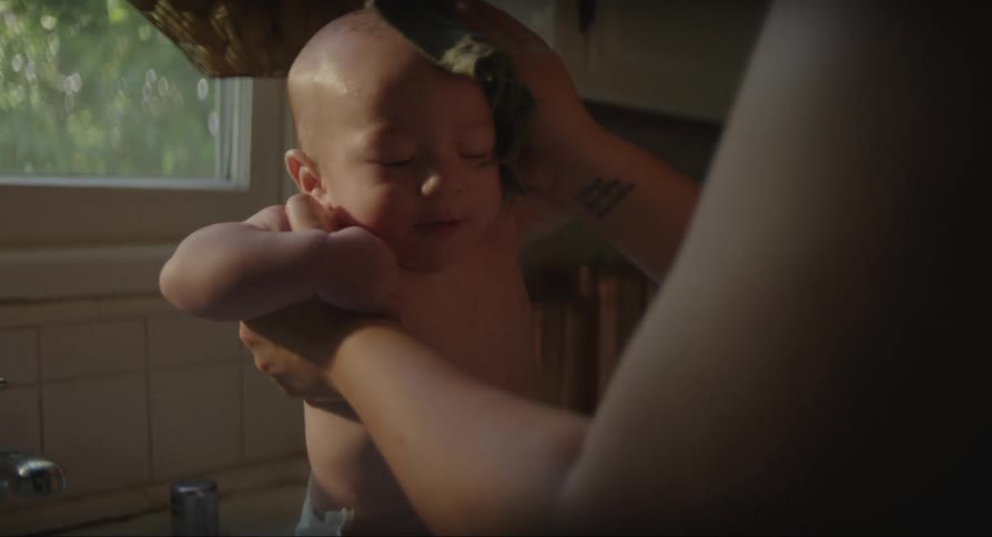 Mother drying up and kissing a wet baby over a bathtub indoors during day time