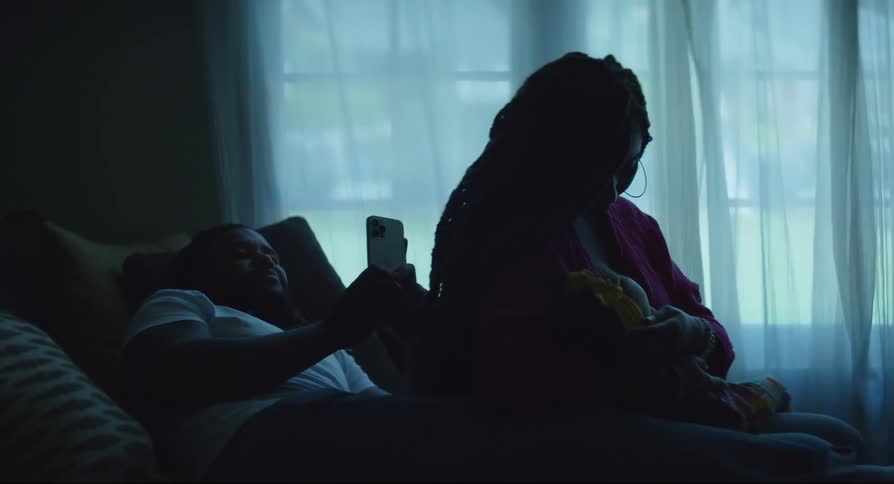 Family sitting on the sofa while the father uses the cell phone and the mother breastfeeds her daughter