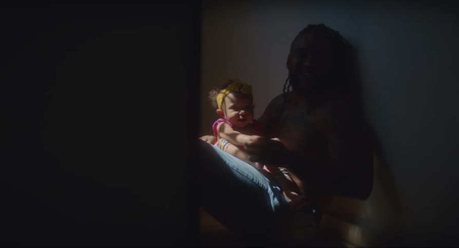 A father holding his baby daughter sitting in a dimly lit hallway in their house
