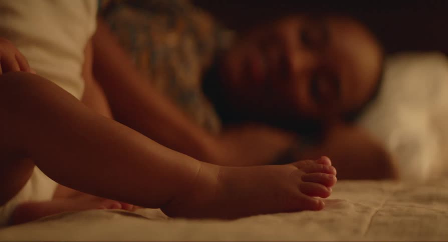 A woman lying in bed smiles and talks to a sitting baby next to her