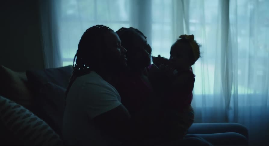 Two black women sitting down indoors playing with a baby on their laps during day time