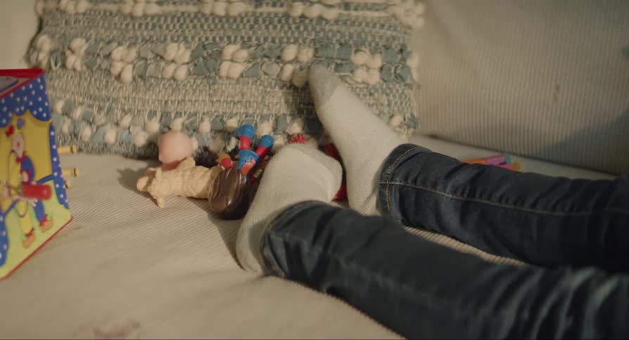 A child lying down in socks and jeans next to toys