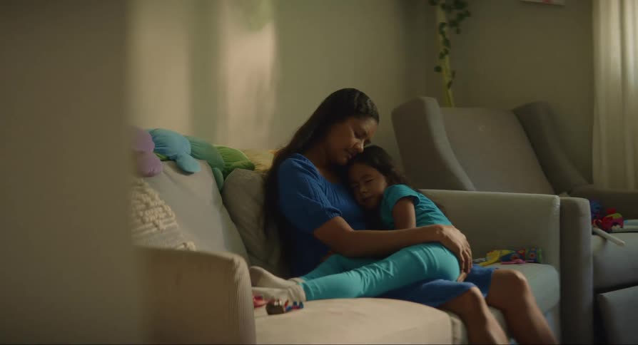 Mother sitting on the sofa with her sleeping daughter in her arms in an indoor setting