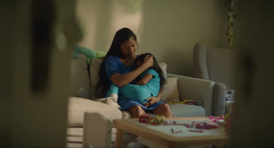 A woman sitting on a couch holding a sad young in her lap while caressing her hair
