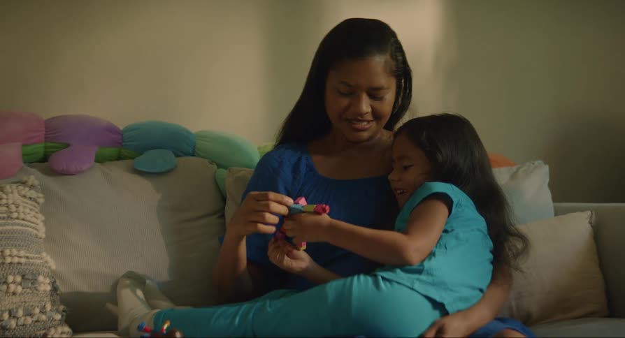 The daughter sits on her mothers lap behind a table where colorful crayons are scattered