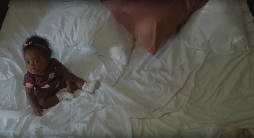 A baby sitting alone in an unmade bed