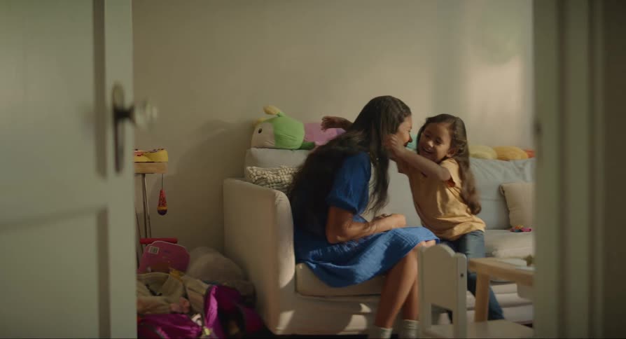 A woman and a young girl sitting on a couch smile and hug each other