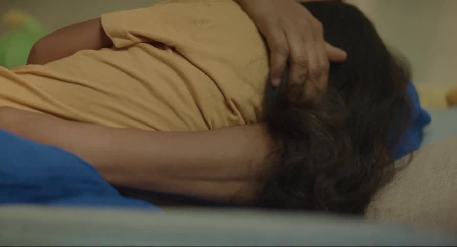 Mother sitting on the sofa with her daughter in her arms gently stroking her hair