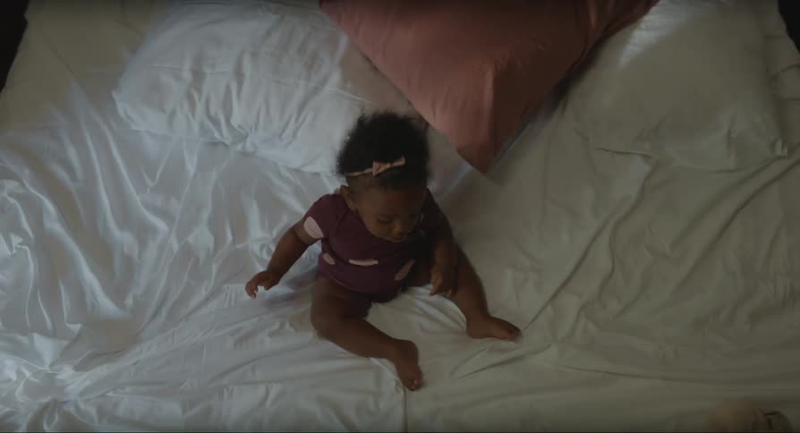 Black baby girl wearing a tiara playing on top of a bed indoors during day time
