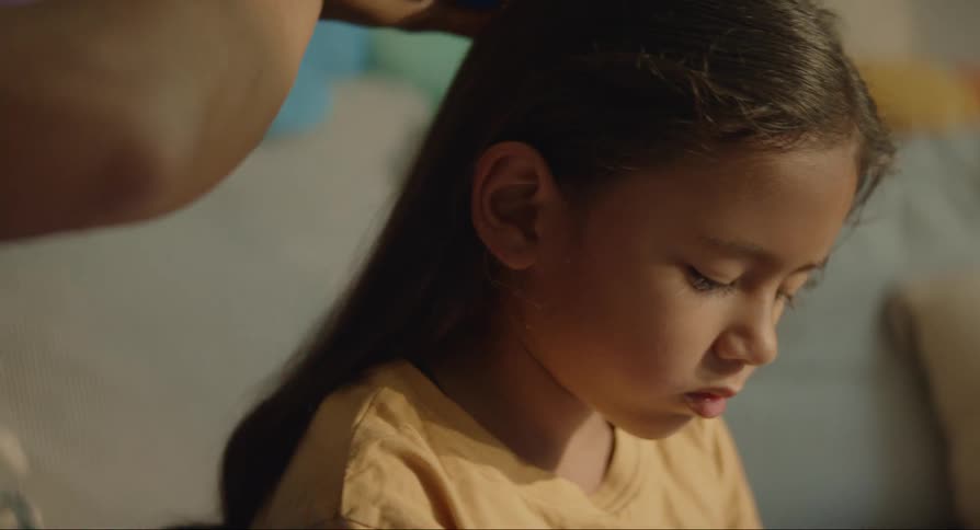 A pair of adult hands comb a young girls hair