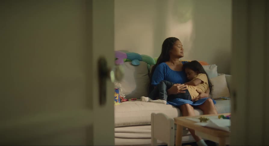 Mother sits in the couch with her sleeping daughter over her lap
