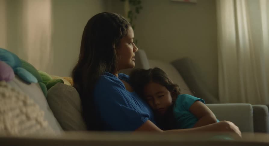 The daughter sleeps in her mothers arms while they sit on the couch in the living room