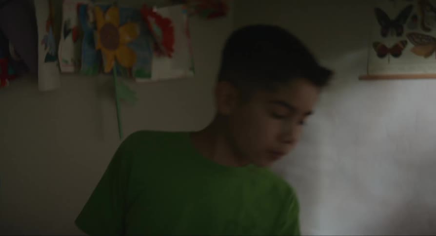 Two boys playing on a sofa and one boy standing and watching