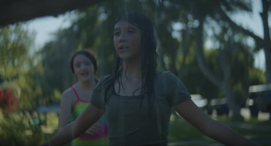 Two adolescents playing with water in an outdoor setting with trees and grass