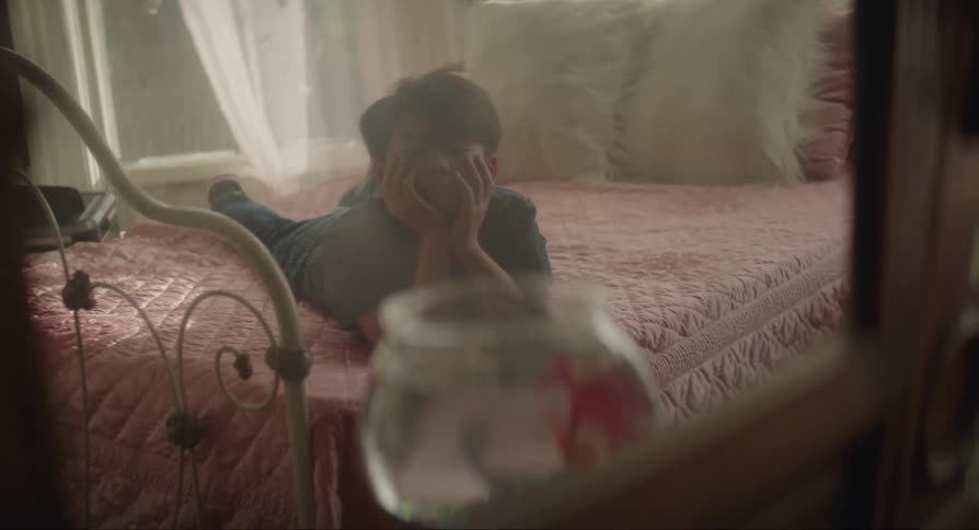 Boy lying on the bed with hands under his chin observing a small aquarium with fish