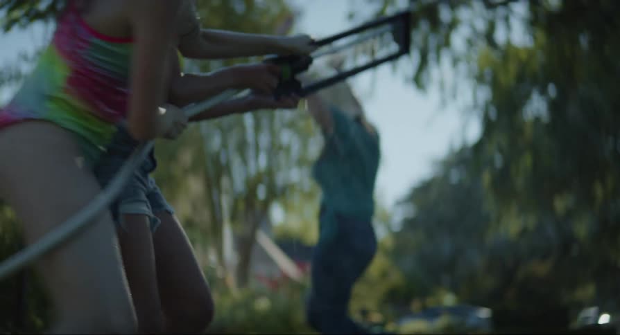 Two teenage girls grab a lawn sprinkler to use it on an adult woman