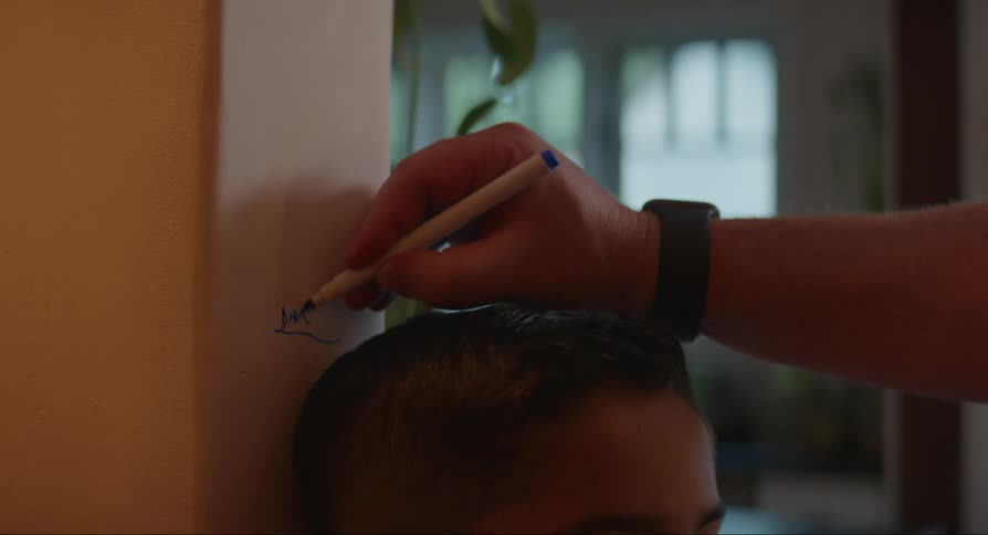 A little boys head being measured on a wall being written on with a marker by his mother