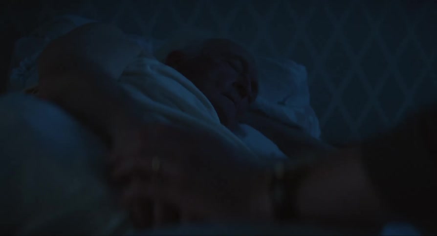 A person holding the hand of an elderly person who is sleeping