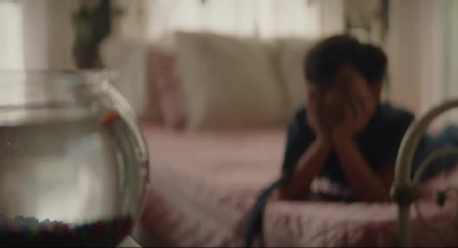 Child lying on the bed and observing a small aquarium with an orange fish