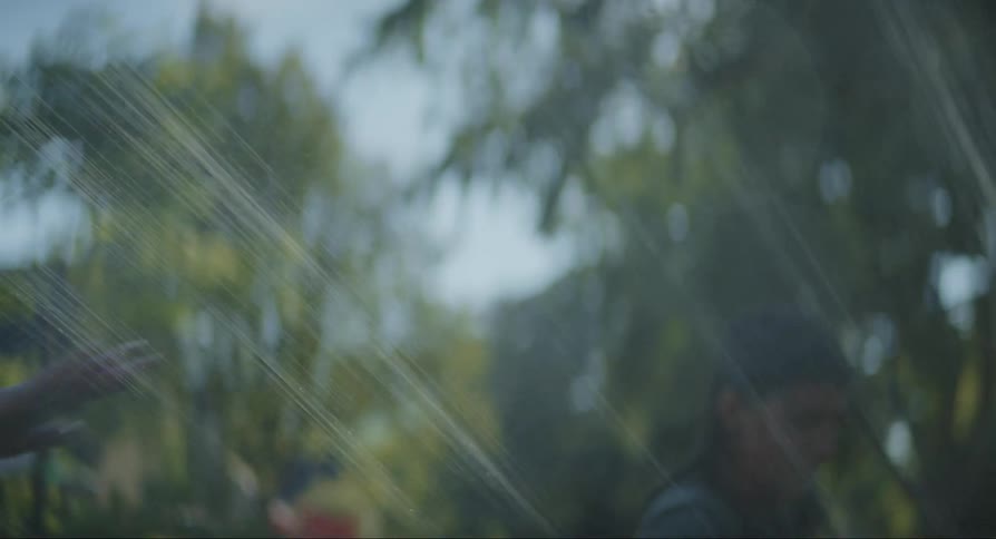 Mother playing with her daughters passing through a water hose while dancing and playing in an outdoor garden