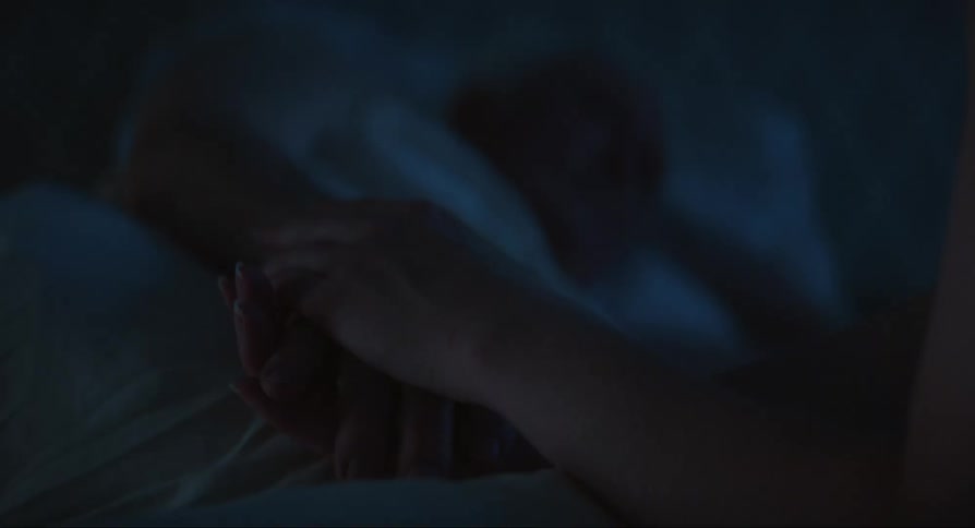 A person is holding the hands of a sleeping man