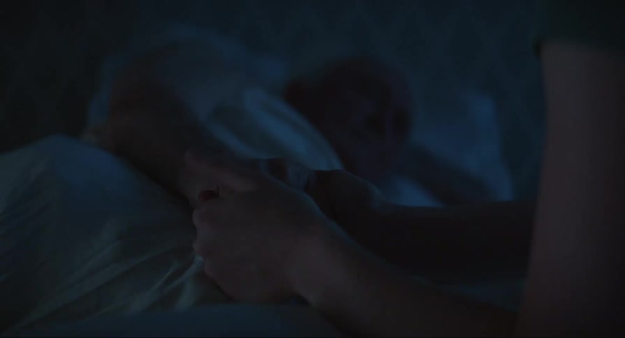 Woman holds old mans hand lying in bed at night